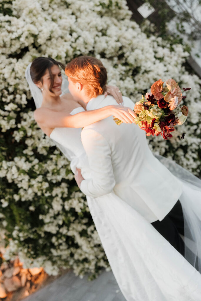 bride and groom twirling around in front of a floral covered wall in jeune perche estate