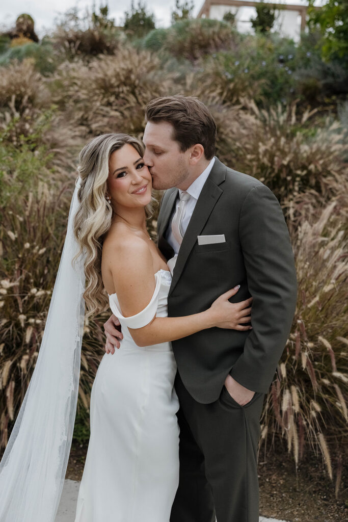 bride and groom posing in front of a lush flower bush at jeune perche