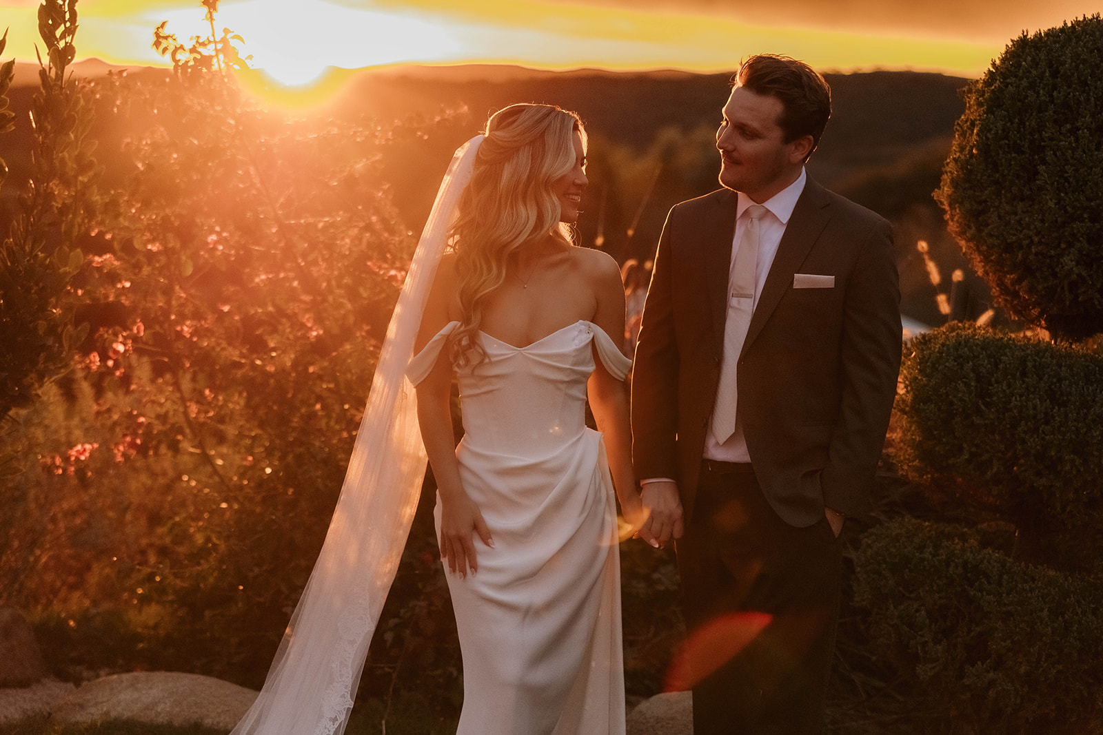 bride and groom holding hands surrounded by rolling hills during golden hour at their california estate wedding venue