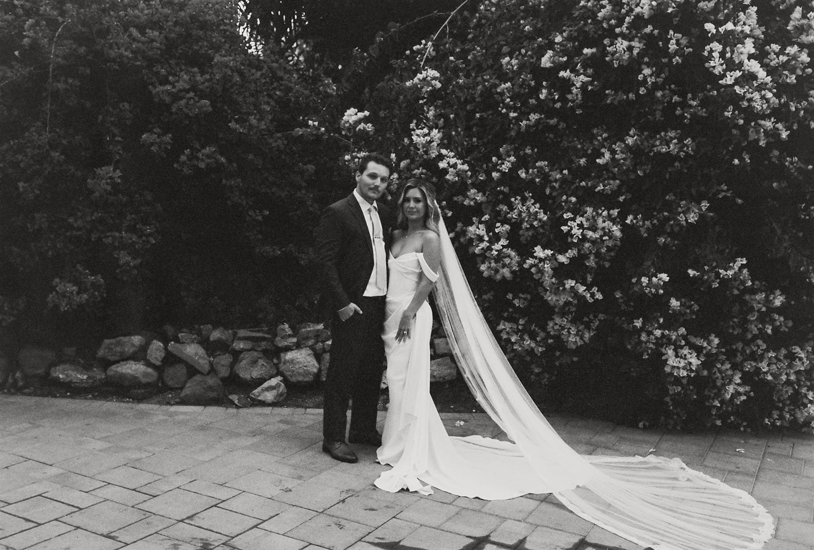 bride and groom posing in front of a lush flower bush at jeune perche
