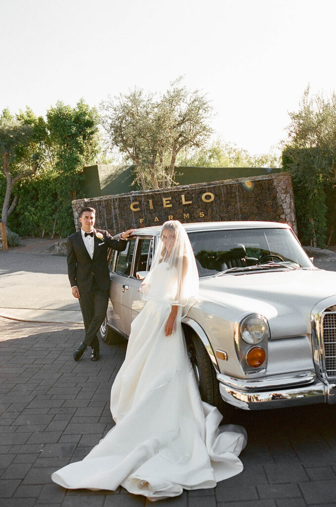 smiley bride and groom in front of a vintage car during their malibu wedding day at cielo farms